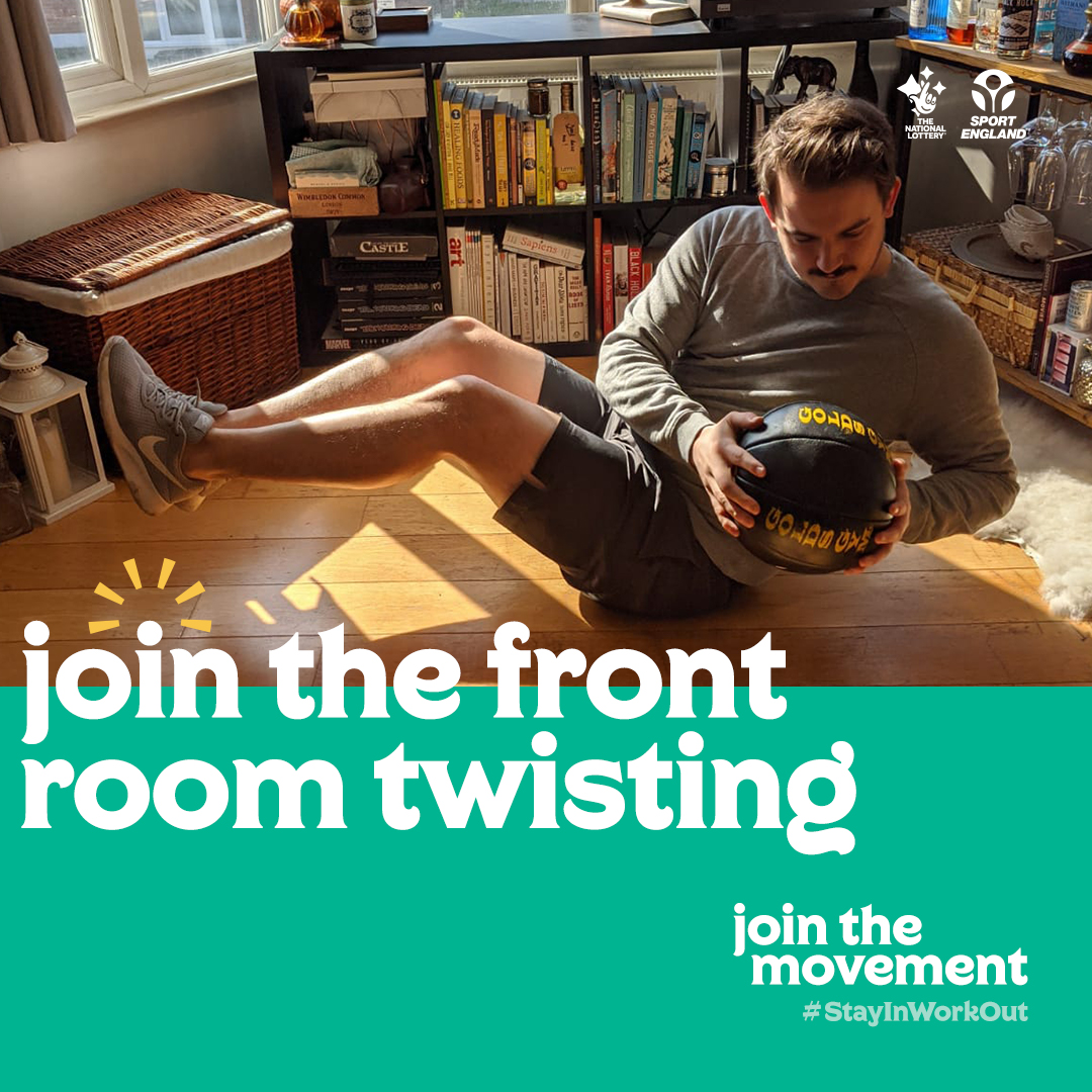 Man sitting on living room floor holding a ball and twisting top half of his body.