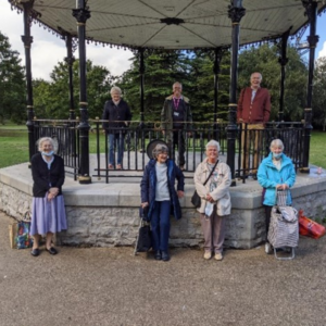 group of older women posing for a photograph on a bandstand in a park.