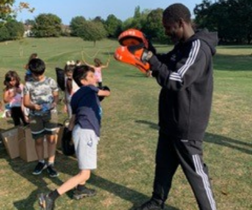 A boxing coach is holding his hands in place for a group of children to practice punching.