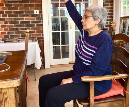 Woman sitting on a chair in front of a laptop on a table and stretching her arm above her head.