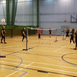 Teenage children playing badminton in a school sports hall.