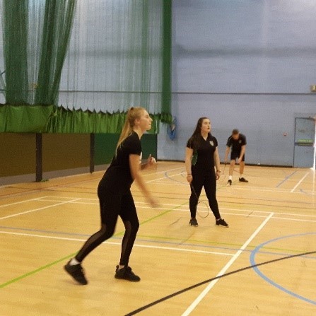 Teenage girls playing badminton in a school sports hall.