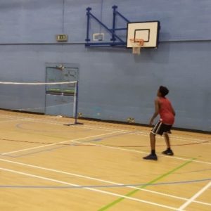 Teenage boy playing badminton in a school sports hall.
