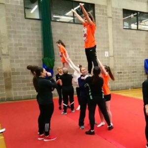 Group of cheerleaders lifting another cheerleader in the air in a school sports hall.