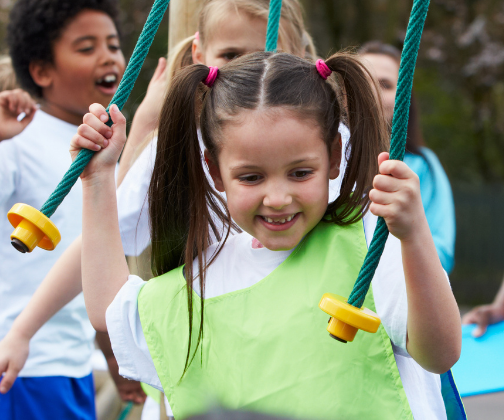 A girl holding on to ropes with each hand to help walk across a piece of playground apparatus.