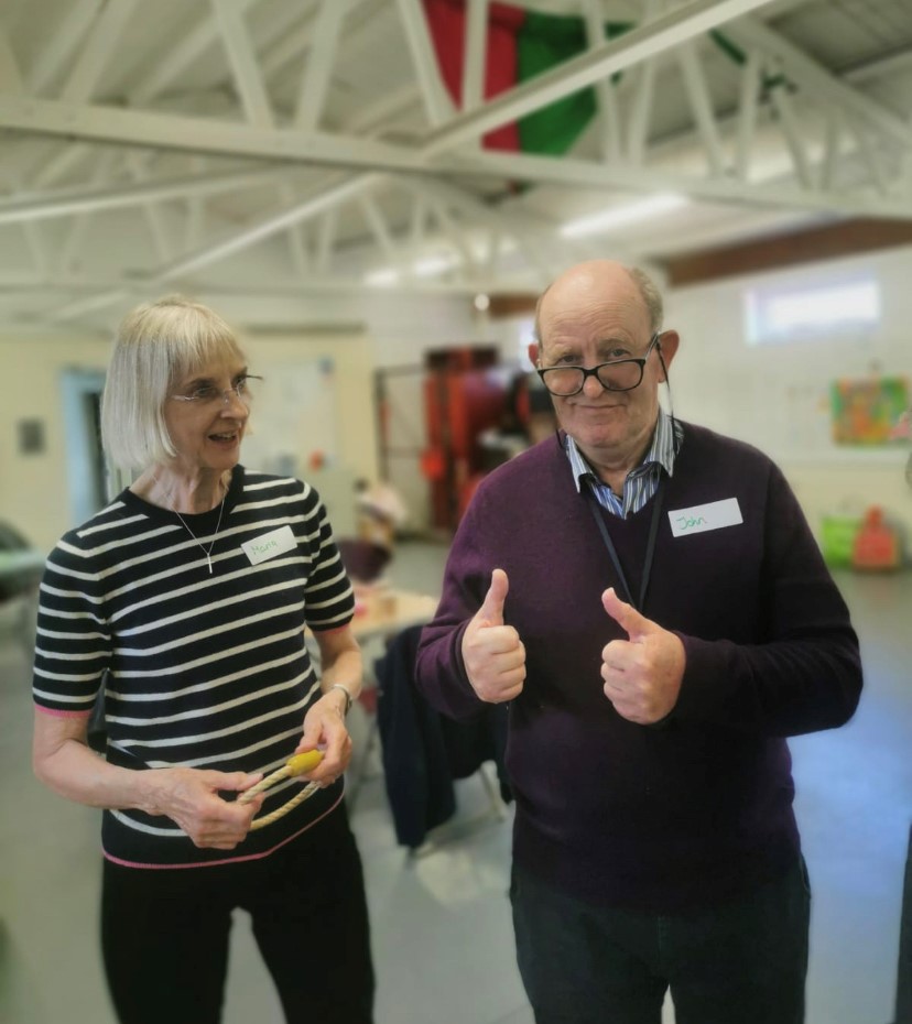 man with dementia holding two thumbs up with a lady by his side