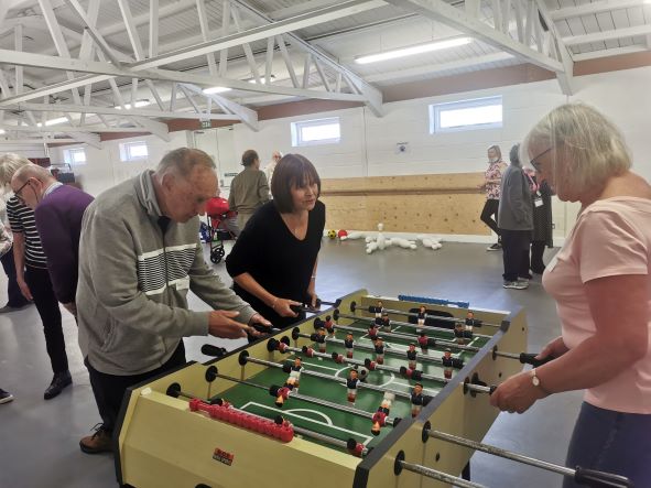 three people playing table football in a hall