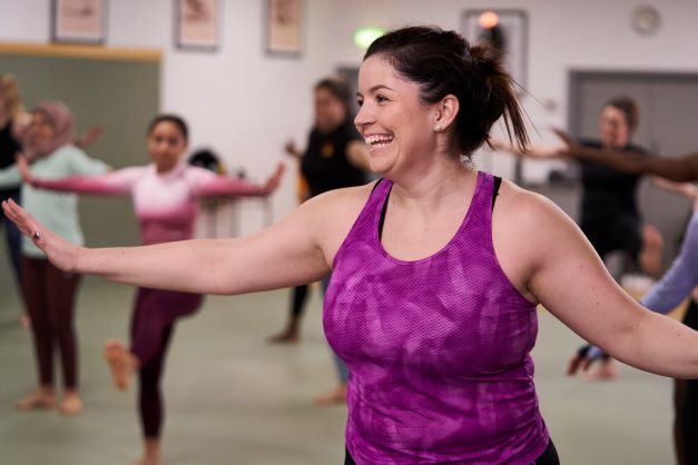 Woman smiling whilst stretching her arms in an exercise class