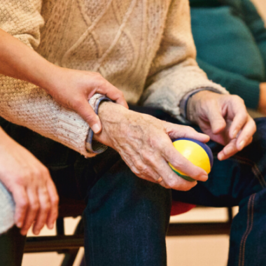 older person sitting in chair, holding ball in his hand