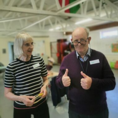 man with dementia holding two thumbs up with a lady by his side