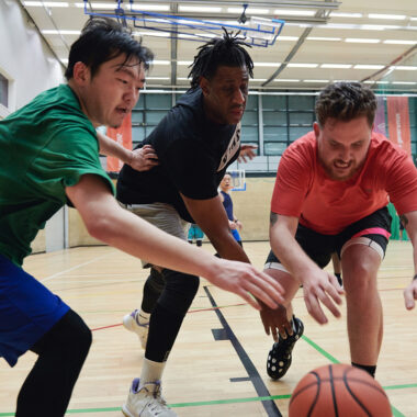 three men in sports hall playing basketball