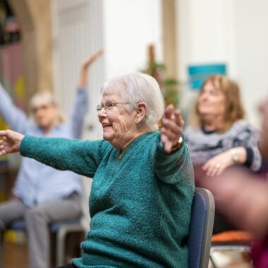 elderly lady seated with her arms in the air, smiling