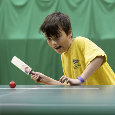 young person playing table cricket in sports hall