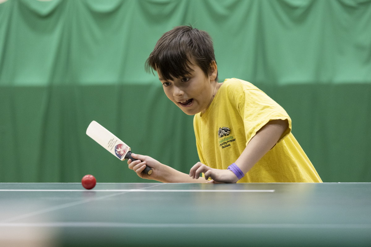 young person playing table cricket in sports hall