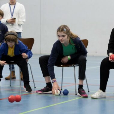 Young people sat in chairs playing boccia in a sports hall