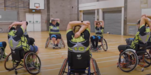 Group of participants using wheelchair to play wheelchair rugby league in a sports hall