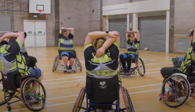 Group of participants using wheelchair to play wheelchair rugby league in a sports hall