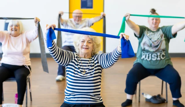 Women in an exercise class sat on chairs holding up resistance bands