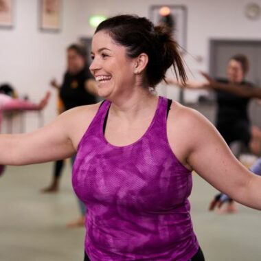 Woman smiling whilst stretching her arms in an exercise class