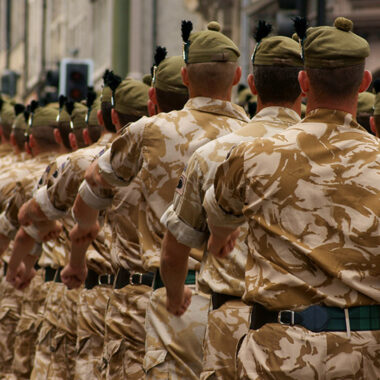 A column of British Army soldiers marching in desert camouflage.
