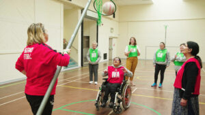 young person in a wheelchair playing netball in a sports hall