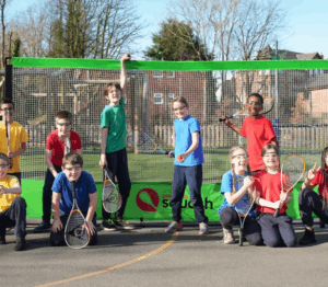 group of young people standing in a school playground holding squash rackets