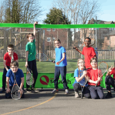 group of young people standing in a school playground holding squash rackets